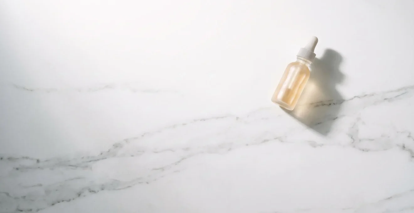 Vue aérienne d'un plan de travail épuré avec une seule bouteille de sérum sur fond blanc minimaliste