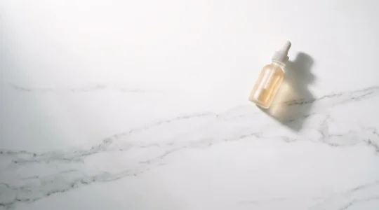 Vue aérienne d'un plan de travail épuré avec une seule bouteille de sérum sur fond blanc minimaliste